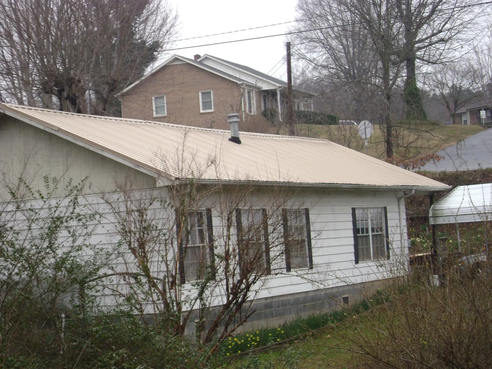 Tan metal roof on a white sided house set into a hillside — Commercial Roofing by Roofing Brothers in Morton